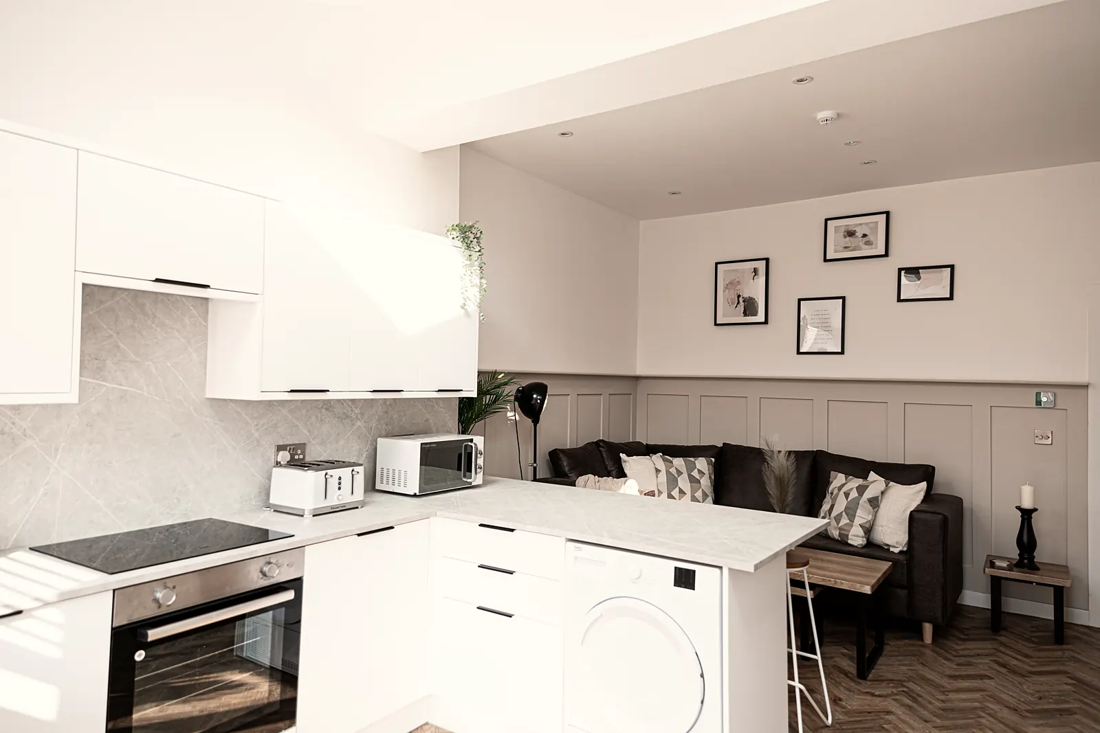 Bright white kitchen with a hob, oven and washing machine beside a sofa area