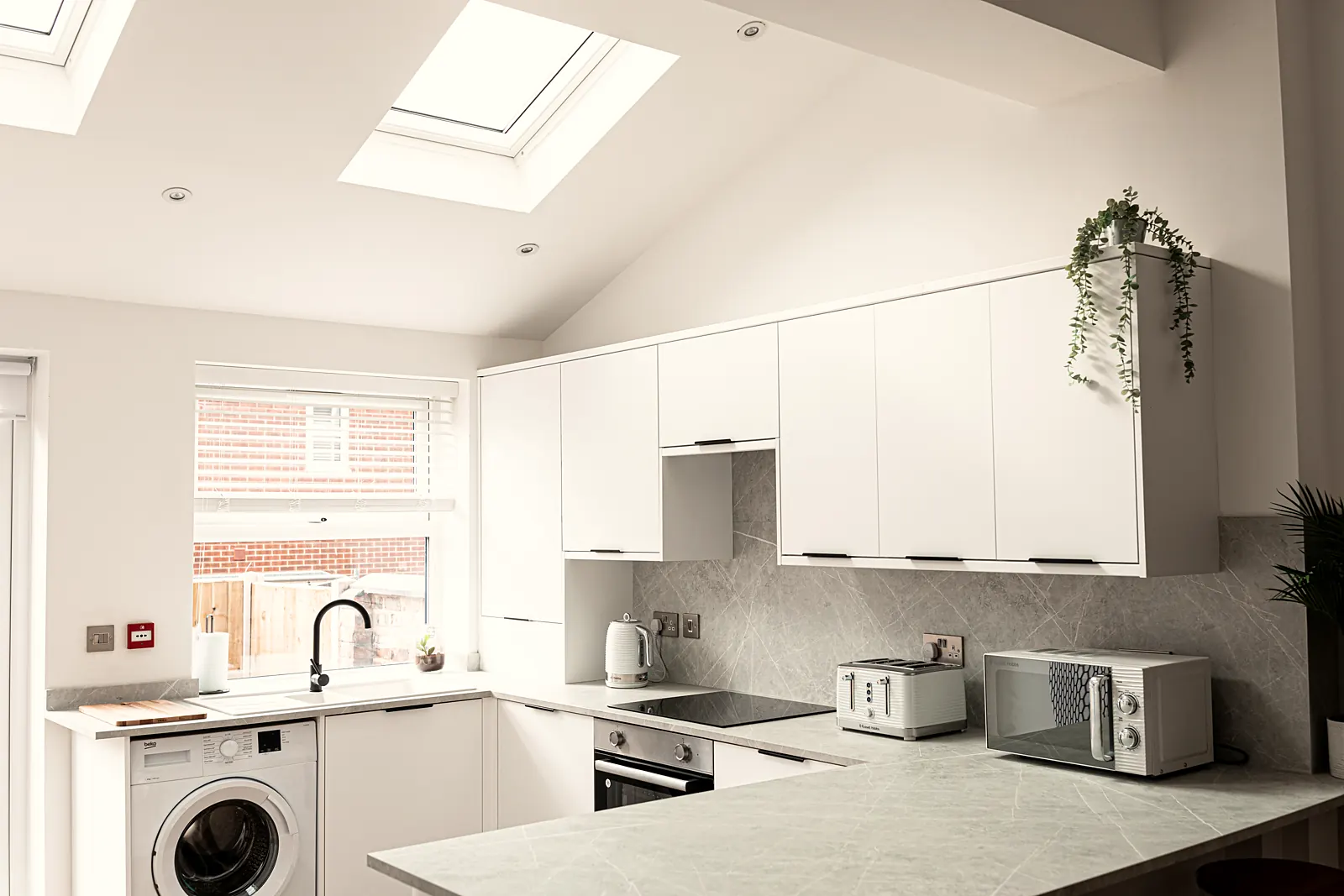 Bright shared kitchen with white units, roof windows and a red fire alarm call point