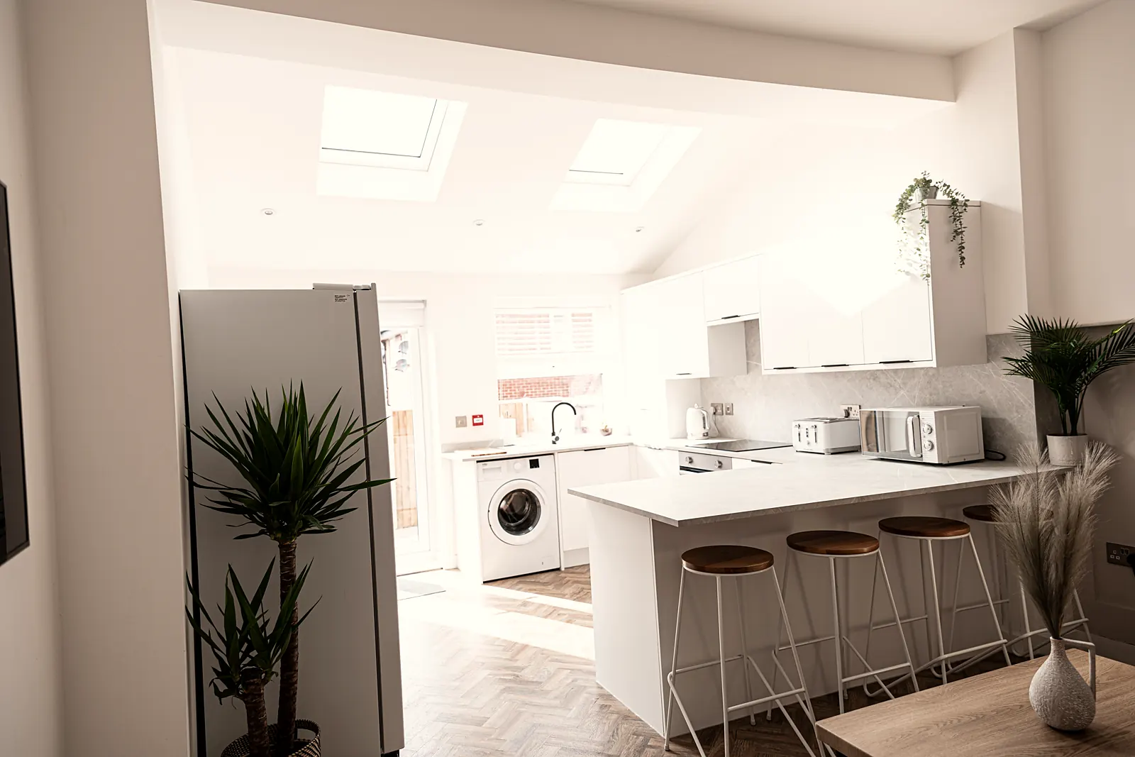 Wide bright shared kitchen and lounge with white units, roof windows and bar stools